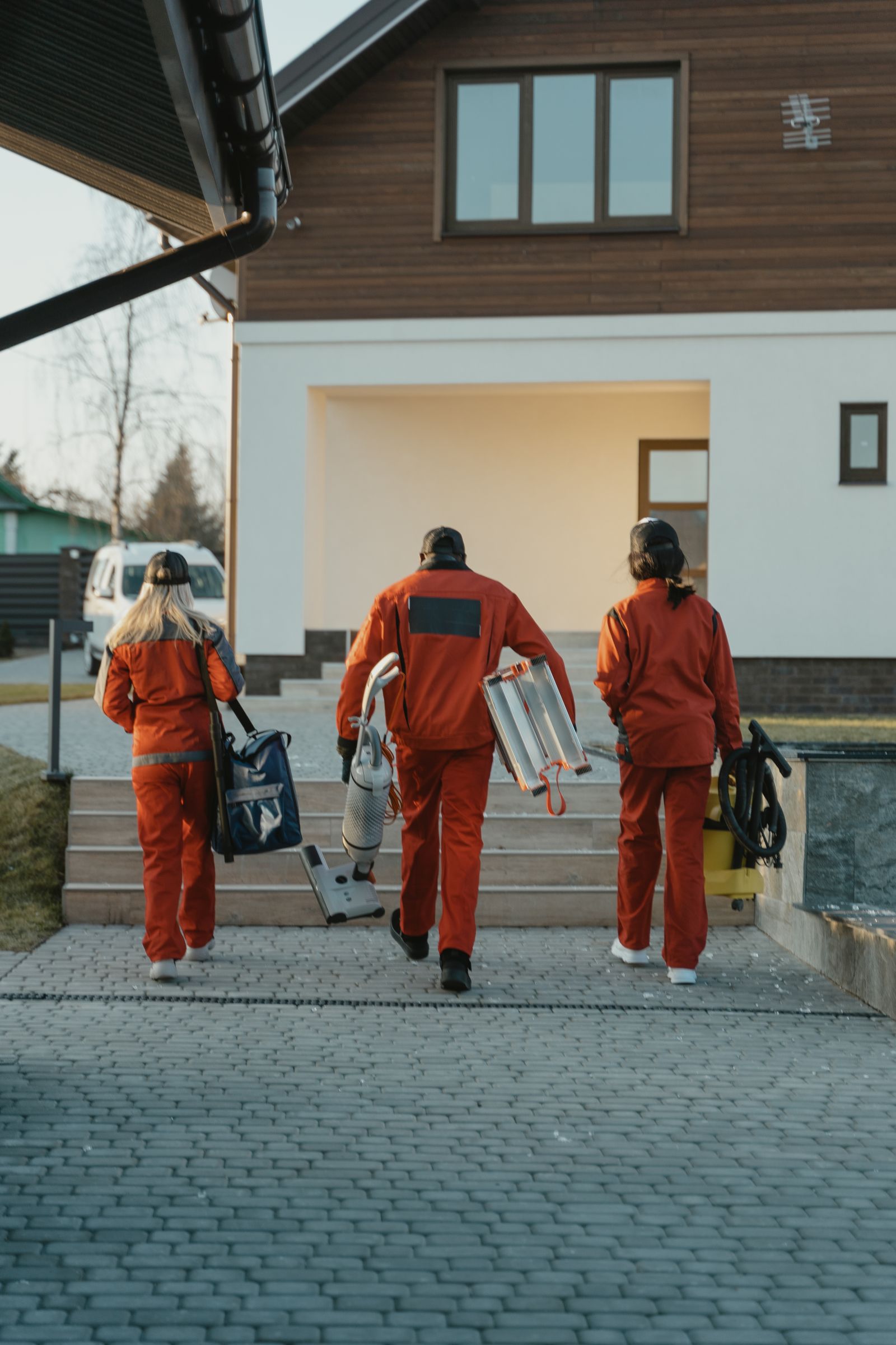 Back view of a cleaning crew in uniform carrying equipment towards a modern house