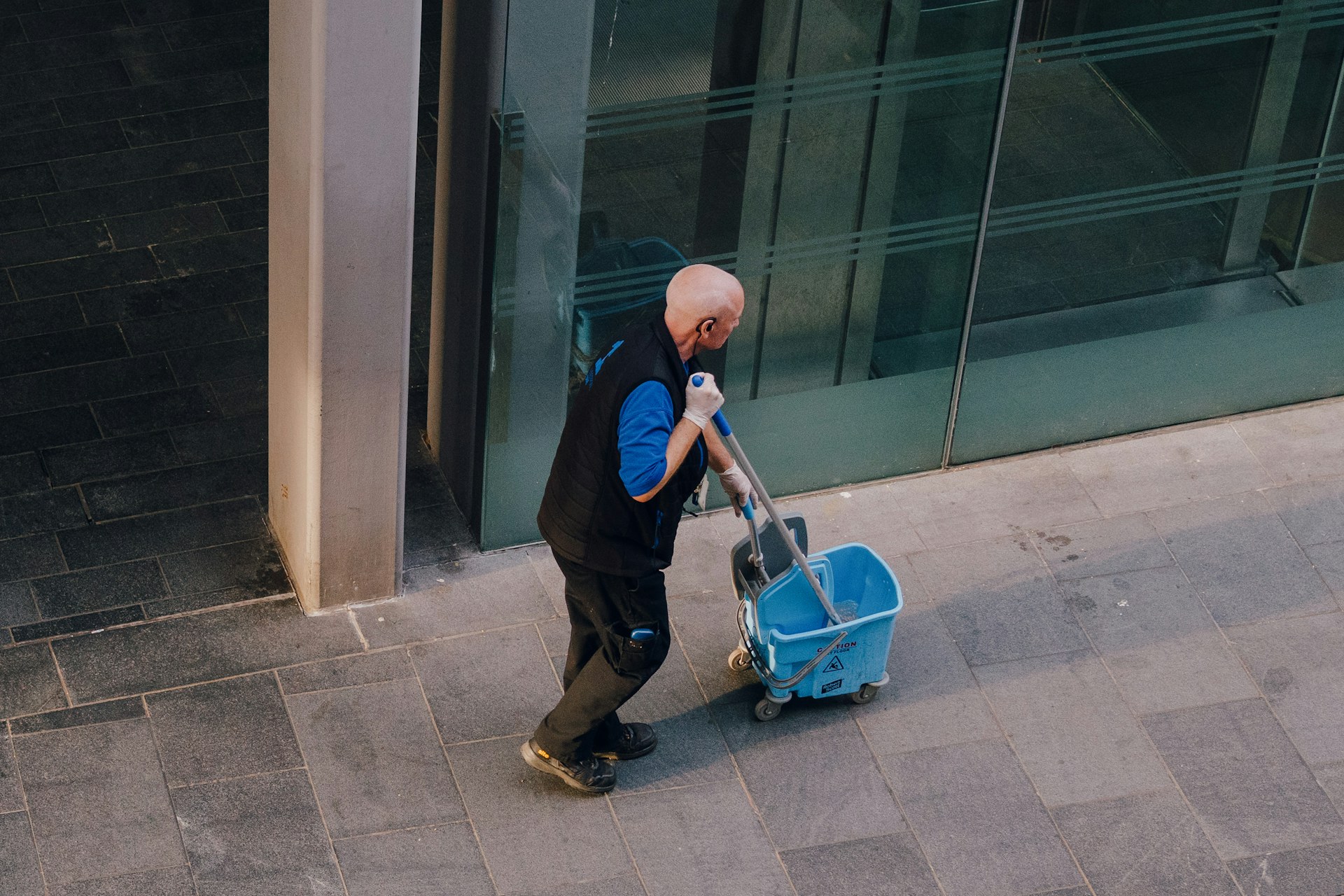 A janitor pulls a cleaning cart along the outside of a commercial building
